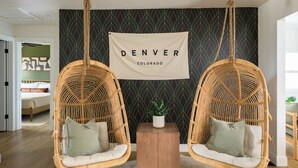 A room with two hanging wicker chairs, a small wooden table with a potted plant, and a banner on the wall. - Spacious + Stylish Home w/HotTub 12min to Downtown (Westminster)