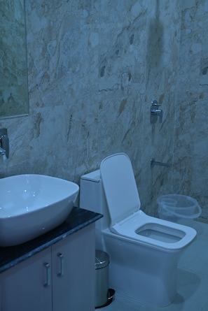 Un baño con pared de mármol, un lavamanos blanco, un inodoro y un cubo de basura.