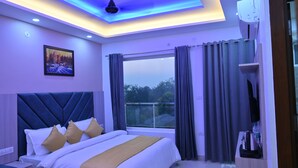 Habitación de hotel moderna con una cama grande, vistas al exterior e iluminación azul en el techo.