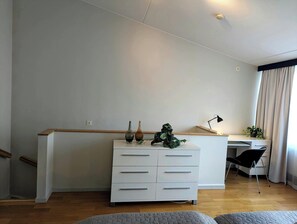 A modern bedroom with a wooden bed frame, a white dresser with drawers, a desk with a chair, and a potted plant.