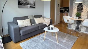 Ein modernes Wohnzimmer mit grauem Sofa, rundem Couchtisch und einer großen Stehlampe.