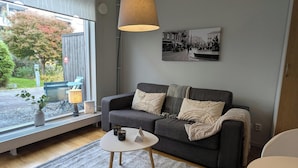 Ein Wohnzimmer mit einem grauen Sofa, einem kleinen weißen Tisch, einem grauen Teppich, einer Lampe und einem Schwarz-Weiß-Foto an der Wand.
