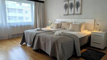 A modern bedroom with a large bed, bedside tables, a nightstand, and a window with curtains.