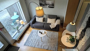 Ein modernes Wohnzimmer mit einem grauen Sofa, einem runden Couchtisch, einer Stehlampe und Blick ins Freie.