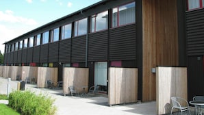 Ein modernes Gebäude mit vielen Fenstern, einer Holzfassade und Außenplätzen.