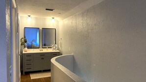 Un baño con una bañera independiente, un lavabo doble con espejo y un pequeño ventilador.