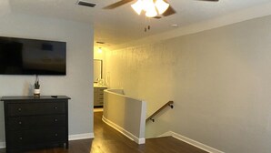 Un dormitorio con cama, cómoda, televisor y escalera que lleva a un baño.