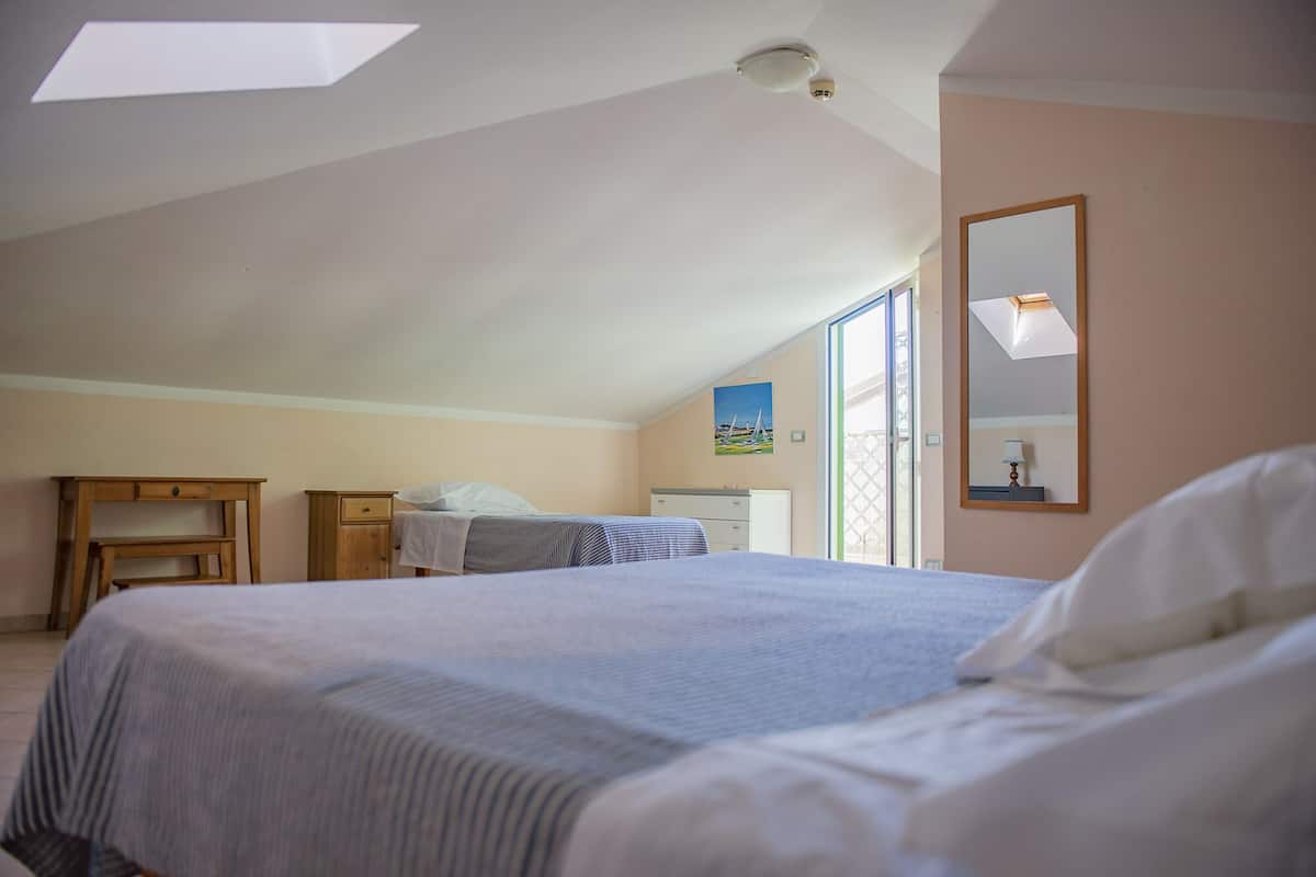 A bedroom with a large bed, a desk, a chair, a dresser, and a window with a view of the outdoors.