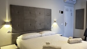 A hotel room with a large bed, two bedside tables, a wall-mounted air conditioner, and a door with a lock. - Hotel l'Etrusco - San Vincenzo (San Vincenzo)