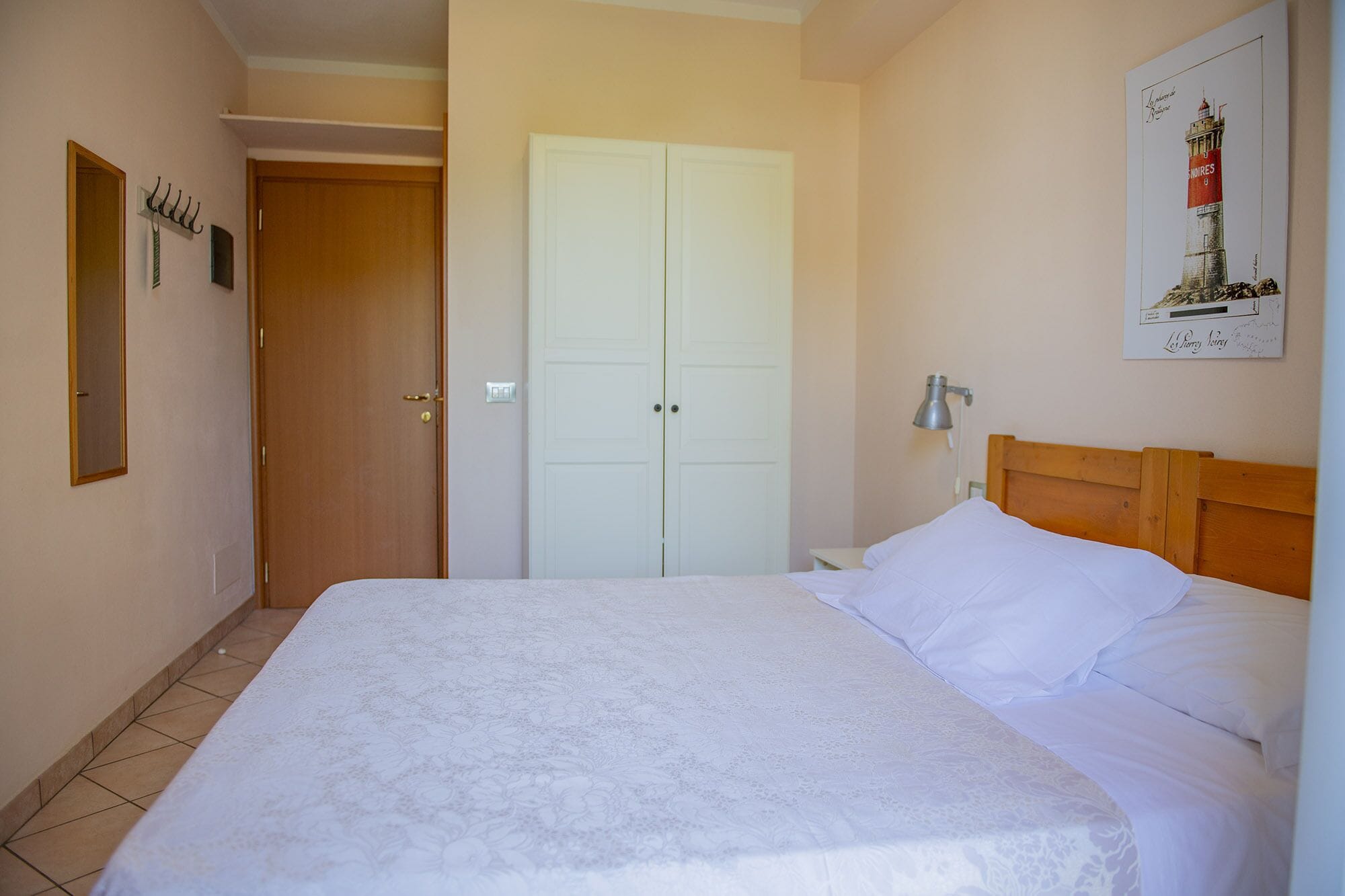 A bedroom with a bed, a nightstand, a lamp, a door, and a wall-mounted picture.
