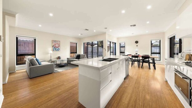 Een moderne keuken met een centraal eiland, een eethoek met een tafel en stoelen, en een zithoek met een bank en een televisie.