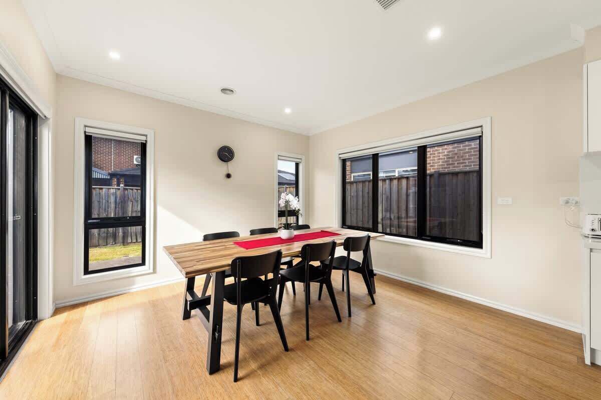 A dining area with a wooden table, black chairs, and large windows.