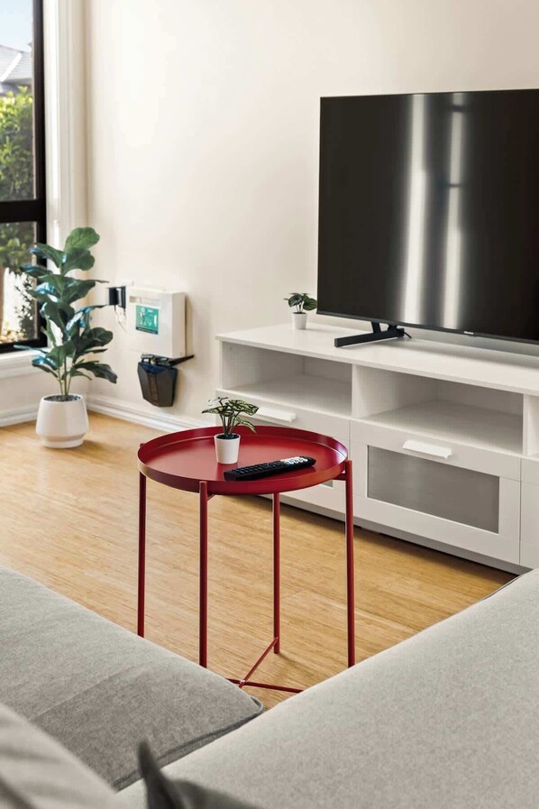 Un salon moderne avec un téléviseur à écran plat, une table basse rouge, un canapé gris et une plante en pot.