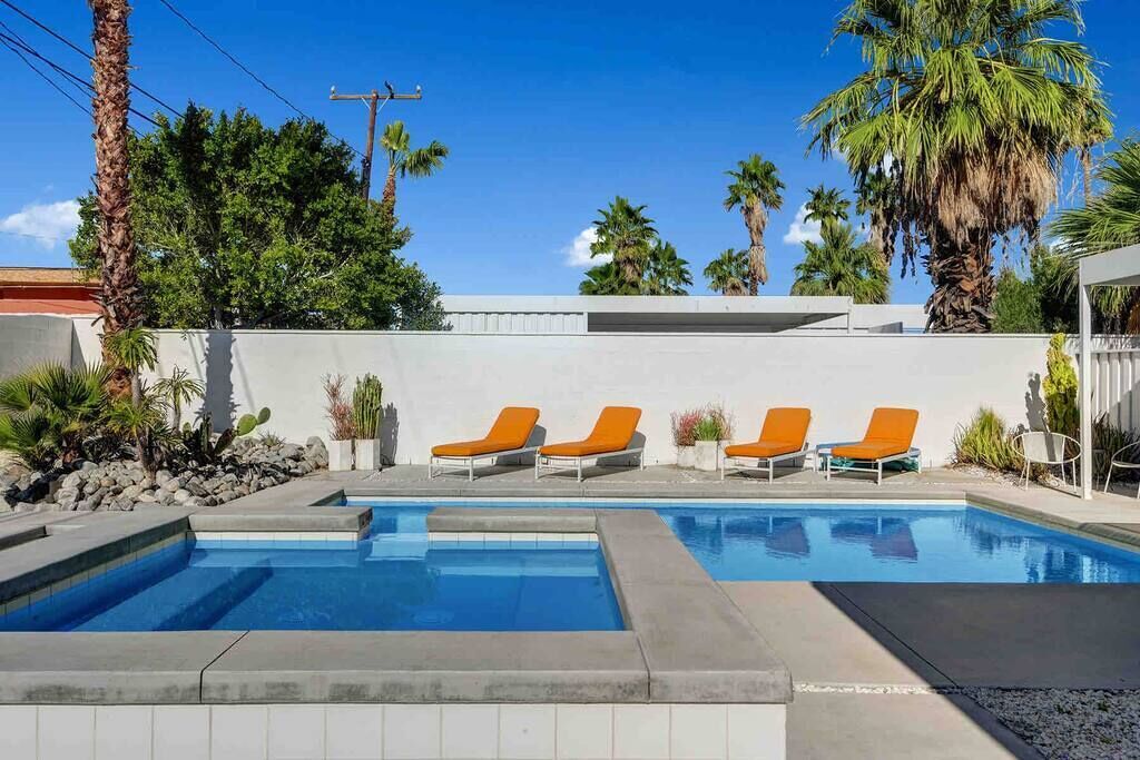 Une piscine avec quatre chaises longues orange et un mur blanc en arrière-plan.