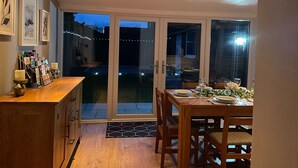 Une cuisine moderne dotée d’une verrière, un coin repas avec une table dressée pour deux personnes, et une vue sur le jardin arrière.