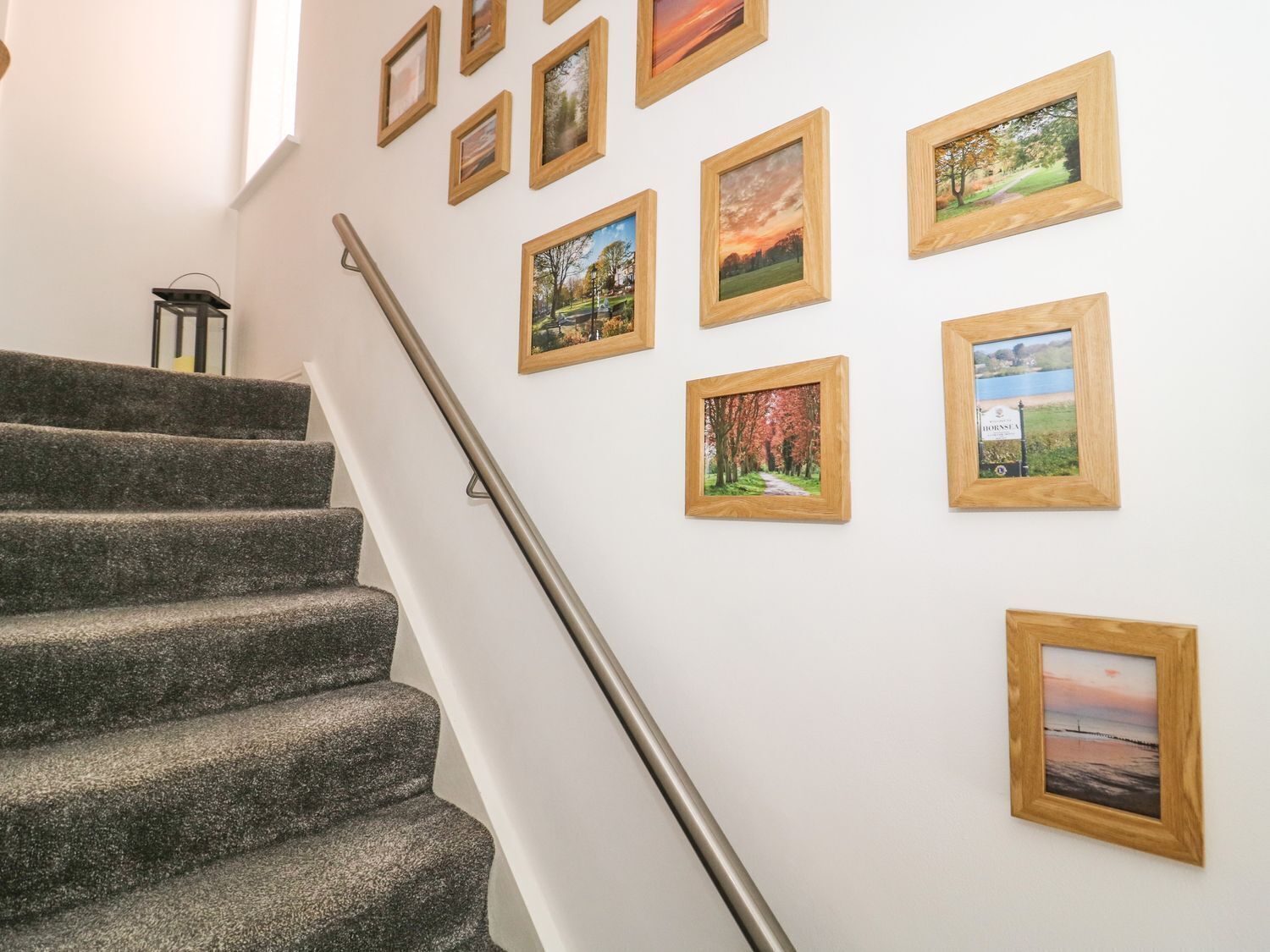 A staircase with a handrail leading to a landing where multiple framed pictures are hung on the wall.