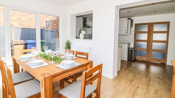 Un coin repas avec une table en bois dressée pour quatre personnes, entourée de chaises dotées de coussins gris.