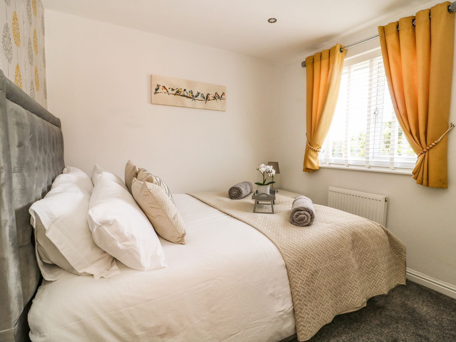 A bedroom with a bed, pillows, a bedside table with a lamp, a window with curtains, and a wall art piece.