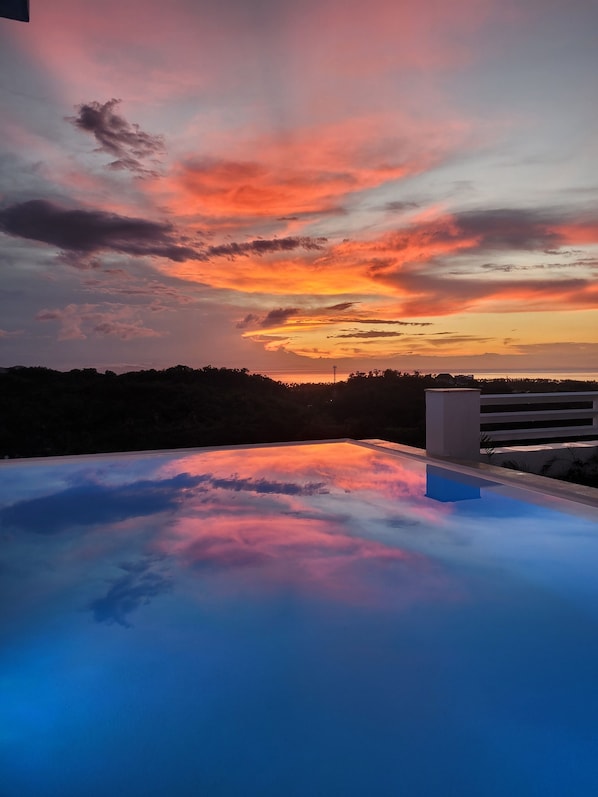A rooftop pool with a view of a sunset over a body of water.