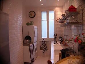 A compact kitchen with white brick walls, a built-in washing machine, a window with frosted glass, and a clock on the wall. - Central Parisian apartment. A 5 minute walk to the Notre-Dame and the Seine (Paris)