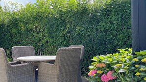 Un espace extérieur aménagé en terrasse, avec des meubles en osier et une table, entouré d’une végétation luxuriante et agrémenté d’une plante en pot ornée de fleurs.
