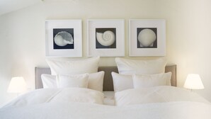 Un lit bien fait, avec du linge de lit blanc et des oreillers, une tête de lit et trois œuvres d’art encadrées au-dessus.