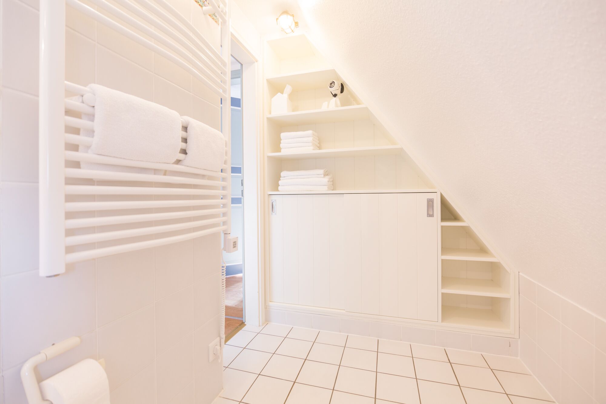 A narrow hallway with a white radiator, a towel rack, and a small storage unit with shelves.