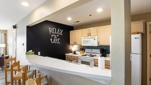 Une cuisine moderne avec un mur d’accent noir, des chaises en bois et un comptoir blanc.