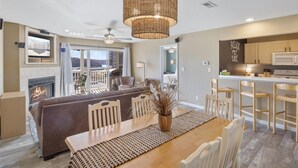 Un vaste espace de vie comprenant un coin salon avec cheminée, une grande table à manger et une cuisine équipée de meubles en bois et d’un bar.
