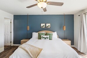 Ein Schlafzimmer mit einem Bett, Deckenventilator, zwei Nachttischen und einer Tür.