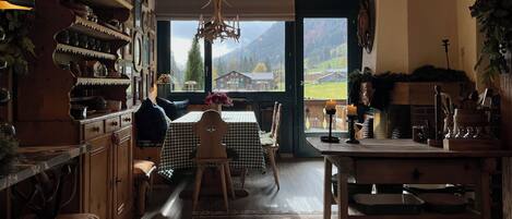 A cozy kitchen with wooden cabinets, a checkered table, and a view of mountains through the open door.
