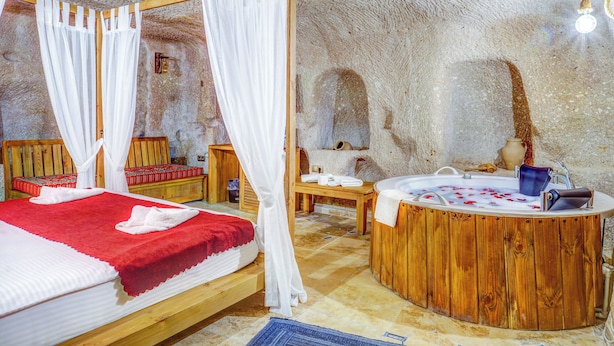 A room with a wooden bed, a wooden bathtub, and a stone wall. - Matiana View Cave Hotel (Nevsehir)