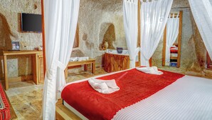 A room with a bed, a wooden desk, a TV, and a stone wall. - Matiana View Cave Hotel (Nevsehir)
