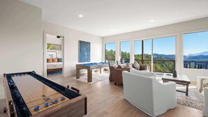 A spacious living area with a pool table, a sofa, and a view of mountains through large windows. - Infinity View Lodge - Indoor pool & mountain views (Sevierville)