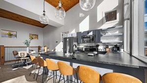 A modern kitchen with a central island, bar stools, and a dining area with a table and chairs. - Infinity View Lodge - Indoor pool & mountain views (Sevierville)