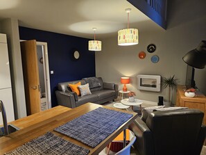 A modern living room with a dark blue accent wall, a leather sofa, a wooden dining table, and a coffee table. - Charming 1-bed Apartment in Newark (Newark)