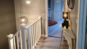 A hallway with a staircase, a ceiling light, a hanging light fixture, and a door leading to another room. - Charming 1-bed Apartment in Newark (Newark)