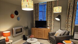 A modern living room with a flat-screen TV, wooden cabinet, leather sofa, and a red knitted pouf. - Charming 1-bed Apartment in Newark (Newark)