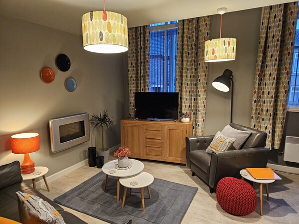 A modern living room with a flat-screen TV, wooden cabinet, leather sofa, and a red knitted pouf. - Charming 1-bed Apartment in Newark (Newark)