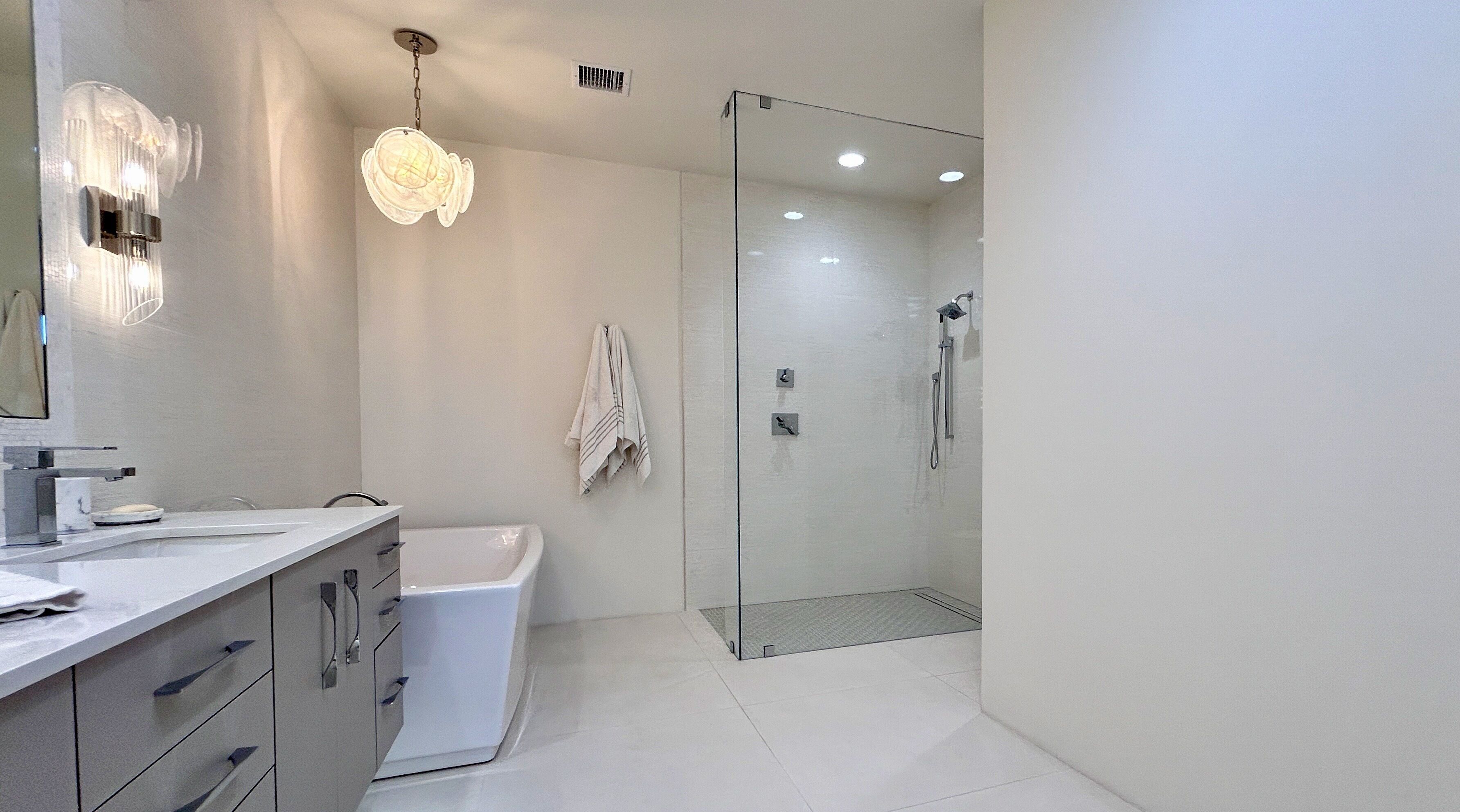 A modern bathroom with a glass shower enclosure, a white bathtub, and a vanity with drawers.