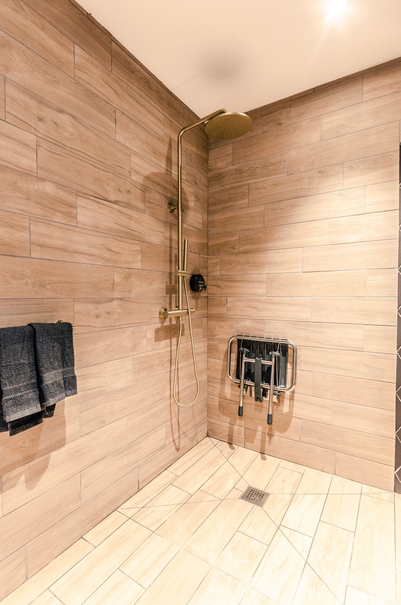 Un espace douche moderne avec des murs et un sol recouverts de carreaux, une douchette à main et un porte-serviettes avec des serviettes.