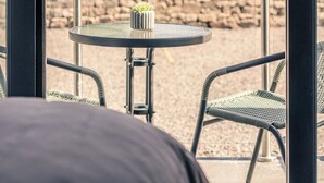 A balcony with a round table and two wicker chairs, overlooking a stone wall and a house. - Sweeney Aviemore One (Aviemore)