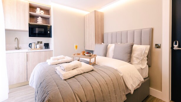 A modern hotel room with a bed, a bedside table with a tray of breakfast, a microwave, and a small kitchenette. - Sweeney Aviemore One (Aviemore)