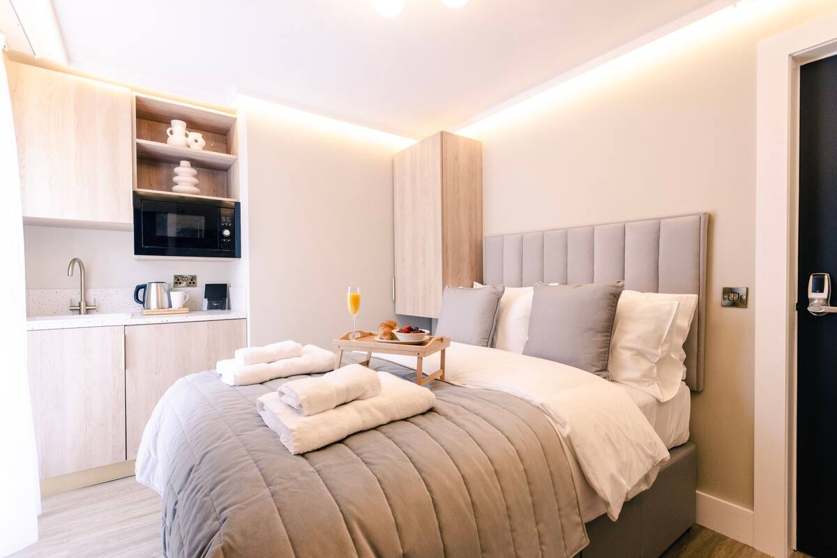 Una habitación de hotel moderna con una cama, una mesita de noche con una bandeja de desayuno, un microondas y una pequeña kitchenette.
