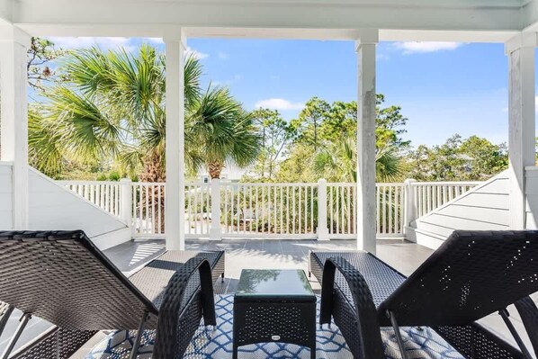 A covered outdoor patio with wicker furniture and a view of palm trees and a white fence. - Beachside home w/ pools & tennis court (Santa Rosa Beach)