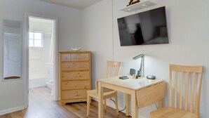 Quarto com escrivaninha de madeira, duas cadeiras, cómoda e televisão de ecrã plano fixada na parede.