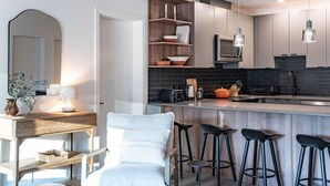 A modern kitchen with a bar area, wooden shelves, and bar stools. - Snowed Inn - Luxurious 3 Bedroom Condo (Revelstoke)