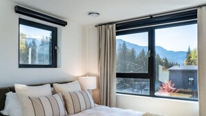 A bedroom with a bed, a window with a view of mountains, and a lamp. - Snowed Inn - Luxurious 3 Bedroom Condo (Revelstoke)