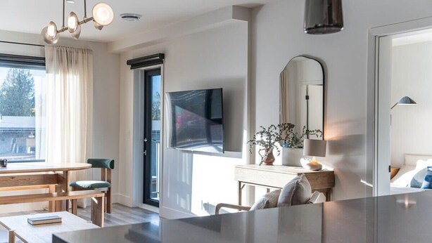 A modern interior with a dining area, a large mirror, a flat-screen TV, and a large window. - Snowed Inn - Luxurious 3 Bedroom Condo (Revelstoke)
