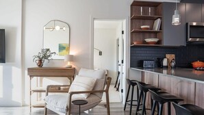 A modern kitchen with a wooden bar, black bar stools, a pendant light, and a microwave. - Snowed Inn - Luxurious 3 Bedroom Condo (Revelstoke)